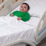 Soleiman portant un pull vert dans un lit médical.
